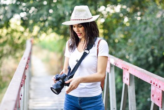 Beautiful hiker young woman taking photographs with a mirrorless camera, wearing straw hat, hiking in the countryside.