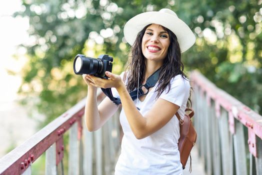 Beautiful hiker young woman taking photographs with a mirrorless camera, wearing straw hat, hiking in the countryside.