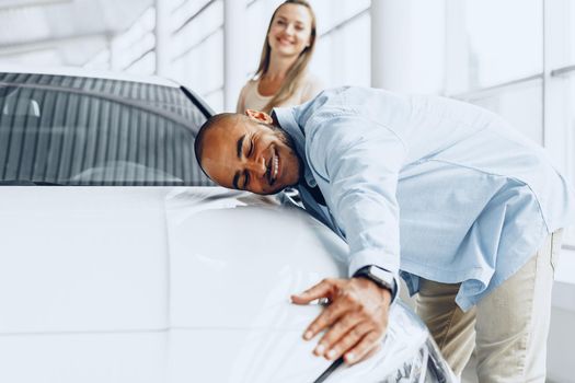 Young couple man and woman hugging their new car in a car shop close up