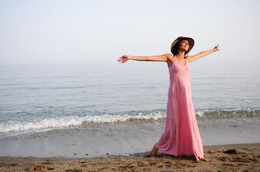 Portrait of a beautiful woman with long pink dress and sun hat on a tropical beach