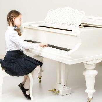 Charming little blonde with long wattled hair in plaits, playing on a white grand piano. In musical school.