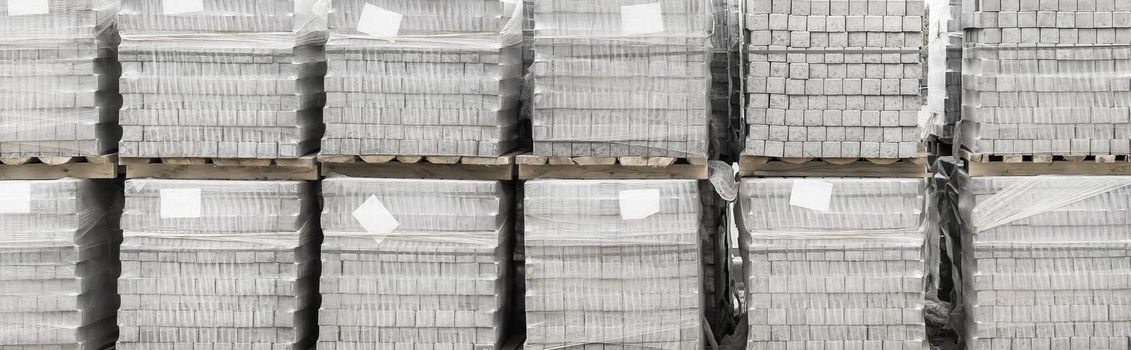 Pile of packaged paving stone slabs industrial material on pallets at construction site.