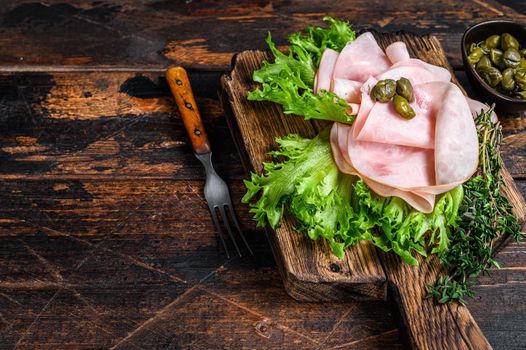 Sliced smoked ham with fresh salad and herbs. Dark wooden background. Top view. Copy space.