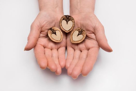 The woman's hands hold three halves of walnut in the form of a heart on a white background, isolated. Nut love concept.
