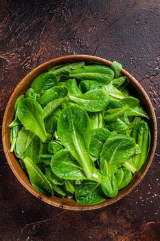 Young romain green salad leaves in wooden plate. Dark background. Top view.
