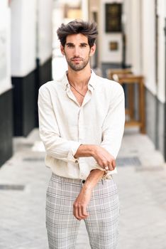 Attractive young man with dark hair and modern hairstyle wearing casual clothes in urban background.