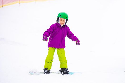 Snowboard Winter Sport. little girl learning to snowboard, wearing warm winter clothes. Winter background.