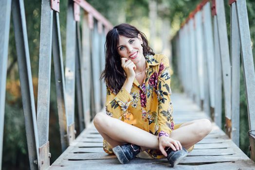 Young woman, wearing flowered dress, hiking in the countryside. Female having fun on a rural bridge.