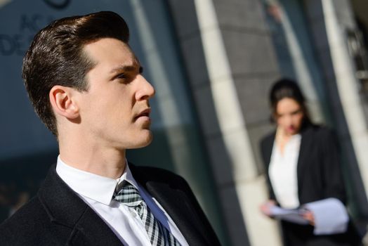 Portrait of attractive young businessman in the city with beautiful businesswoman in the background