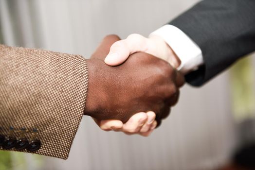 Black businessman shaking hands with a caucasian one wearing suit in a office. Close-up shot