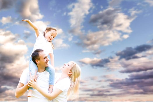young happy family having fun outdoors, dressed in white and with blue sky in background