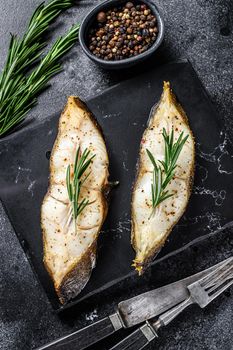 Halibut fish steak with rosemary. Black background. Top view.