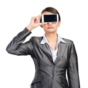 Portrait of pretty woman covering her eyes with smartphone. Businesswoman showing mobile phone with blank screen. Corporate businessperson isolated on white background. Mobile communication layout