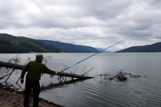 a man is fishing with a fishing rod on a mountain lake in the evening.