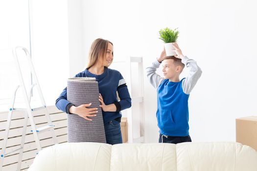 Young cute single mother and son are happy about the move to new house holding a pot of greens and carpet in their hands. Concept of housewarming and family space extensions