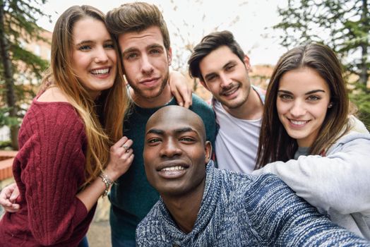 Multiracial group of friends taking selfie in a urban park with a black man in foreground