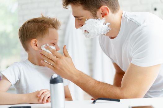 Father teaches his little son how to shave face in bathroom