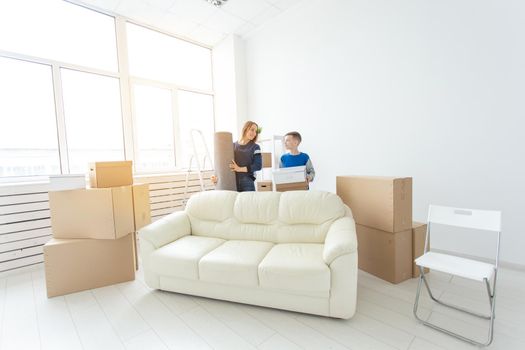 Young cute single mother and son are happy about the move to new house holding a pot of greens and carpet in their hands. Concept of housewarming and family space extensions