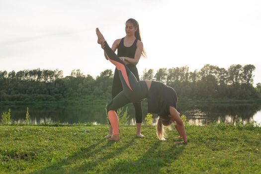 Harmony and healthy lifestyle concept - Young slim women in sportswear practicing yoga outdoors