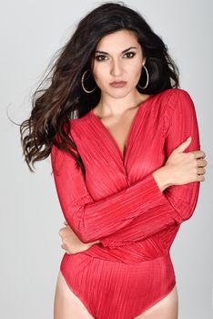 Young woman wearing red body and earrings on white background. Brunette girl with long hair and wavy hairstyle looking to camera. Studio shot.