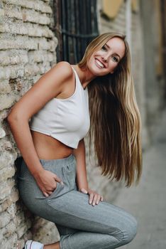 Smiling blond girl wearing casual clothes in the street. Young woman with straight hair in urban background.