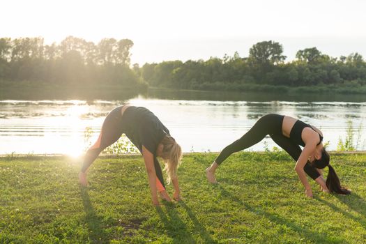 Harmony and healthy lifestyle concept - Young slim women in sportswear practicing yoga outdoors