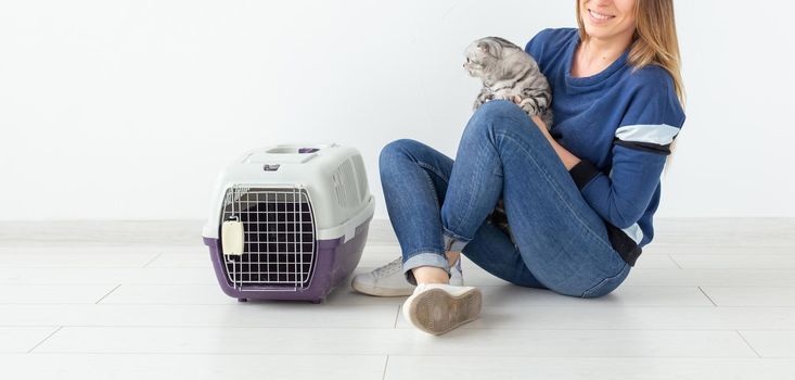 Charming positive young woman holds in her hands her beautiful gray fold scottish cat sitting on the floor in a new apartment. Pet concept. Copyspace