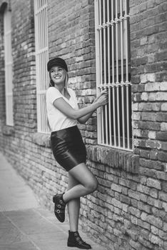 Young blonde woman smiling near a brick wall. Girl with blue eyes wearing t-shirt, skirt and cap.