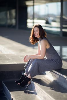 Beautiful young woman, model of fashion, sitting in urban background. Girl smiling.