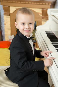 Beautiful little boy in a strict black suit , white shirt and tie.He sits at the piano keys.