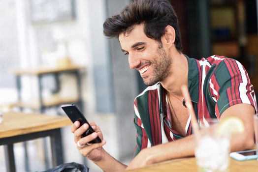 Young man using smartphone in an urban cafe. Male wearing casual clothes.