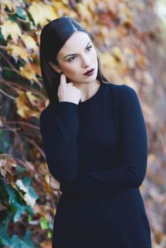 Beautiful young woman, model of fashion, wearing black dress in urban background with autumn colors. Very straight hair styling