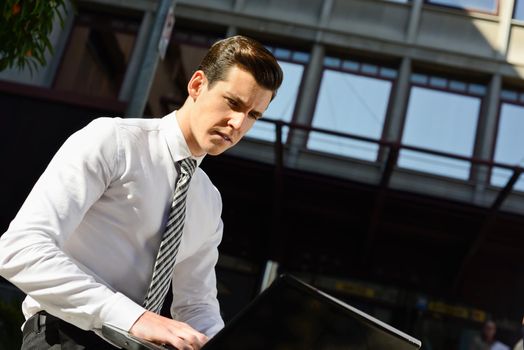 Portrait of attractive young businessman typing in a laptop computer in urban background