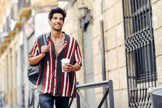 Young male traveler enjoying the streets of Granada, Spain. Man using earphones carrying backpack and a take-away glass.