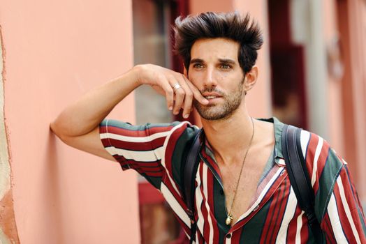 Handsome young man with dark hair and modern hairstyle wearing casual clothes in urban background.