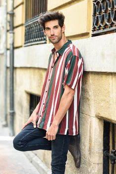 Attractive young man with dark hair and modern hairstyle wearing casual clothes in urban background.