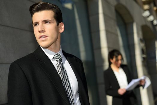 Portrait of attractive young businessman in the city with beautiful businesswoman in the background