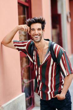 Smiling young man with dark hair and modern hairstyle wearing casual clothes in urban background.