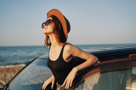 cheerful woman in sunglasses and a hat on the ocean near the car. High quality photo
