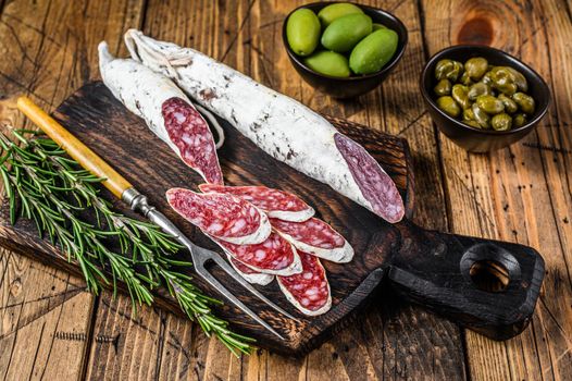 Spanish tapas Fuet Salami sausage slices with olives and rosemary on a wooden board. wooden background. Top view.