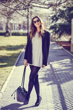 Portrait of beautiful woman smiling, wearing casual clothes, bag and sunglasses in urban background