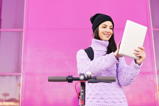 Woman in her twenties with electric scooter using digital tablet outdoors. Lifestyle concept.