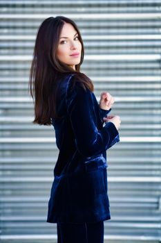 Woman wearing blue suit posing near a modern metal building. Lifestyle concept.