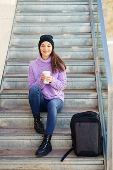 Woman in her twenties taking a coffee break sitting on some steps in the street. Lifestyle concept.