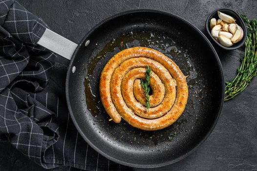 Fried spiral sausages with garlic and seasoning in a pan. Black background. Top view. Copy space.