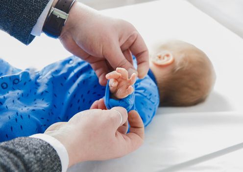 Dad's hands roll up sleeves on baby's hand, close-up. Newborn child in the hospital, love and care of the parent's dad.