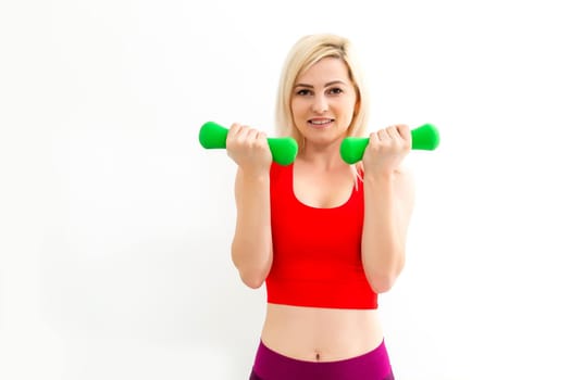 Smiling athletic woman pumping up muscles with dumbbells on white background