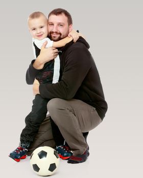 little boy who loves to play football embraces his beloved father.On a gray background.