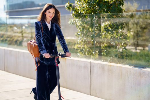 Young business woman wearing blue suit using electric scooter. Lifestyle concept.