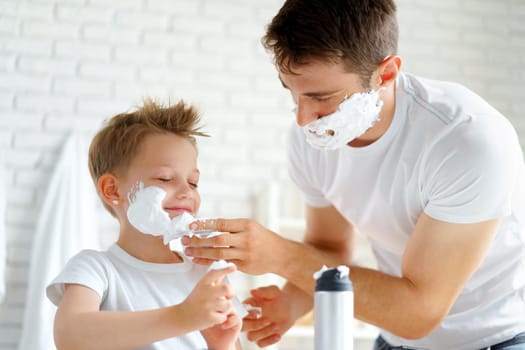 Father teaches his little son how to shave face in bathroom